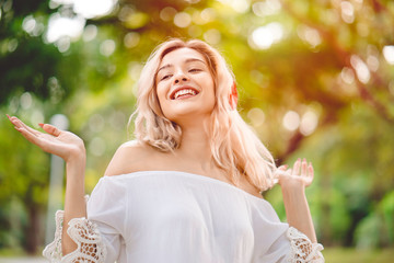 Happy woman listening online music from headset which connecting Bluetooth from a smartphone.  Happiness with smiling face, freedom and dancing in a park during summer with trees background