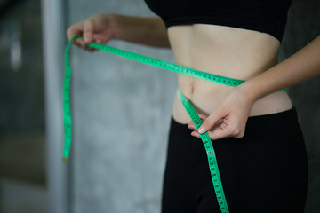 Young woman using green tape or waistline measure her waist at gym or fitness, under diet and fat...