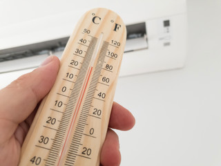 Thermometer and temperature measuring with modern air condition unit on a white wall inside the living room.