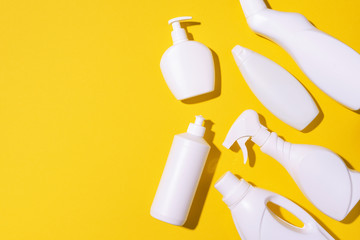 Detergent bottles and chemical cleaning supplies on yellow background. Top view. Copy space. Flat lay.