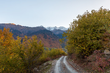 Fototapeta na wymiar Panoramic view of a mountain road passing through mountains and peaks in the snow, visible in the distance, in the mountainous part of Georgia - Svaneti at sunset