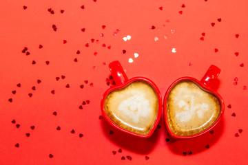 Red pair of cups of coffee in shape of heart on red background with sparkles hearts. Valentine's day concept, symbol of love. Top view, copy space