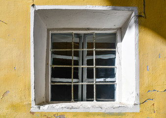 Fototapeta na wymiar Close-up of the small, square window of an abandoned house with yellow wall background, Italy