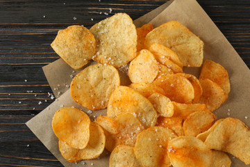 Potato chips with salt and craft paper on wooden background, top view