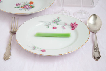 On big beautiful plate lies a small stem celery near beautiful spoon and a fork