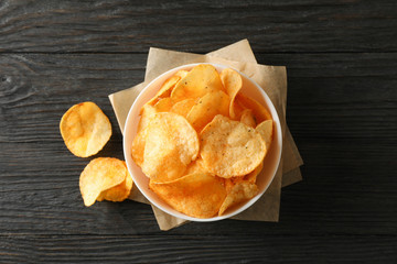 Potato chips in a bowl, craft paper on wooden background, space for text. Top view