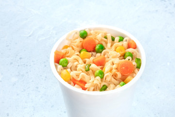 Ramen cup close-up, instant soba noodles in a plastic cup with green peas and carrot slices