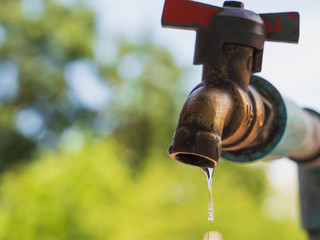 Old metal water tap with water drop as natural green background in concept of water conservation.