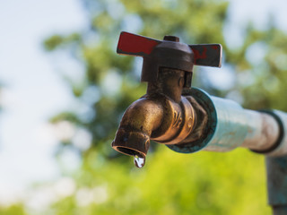 Old metal water tap with water drop as natural green background in concept of water conservation.