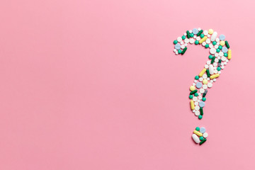 Composition of pills and capsules on a pink background in the form of a question mark....