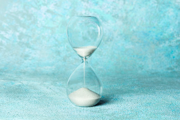 Time is running out concept. An hourglass with sand falling through, on a teal blue background with...