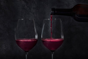 Wine poured into glasses from a bottle, on a dark background with a place for text