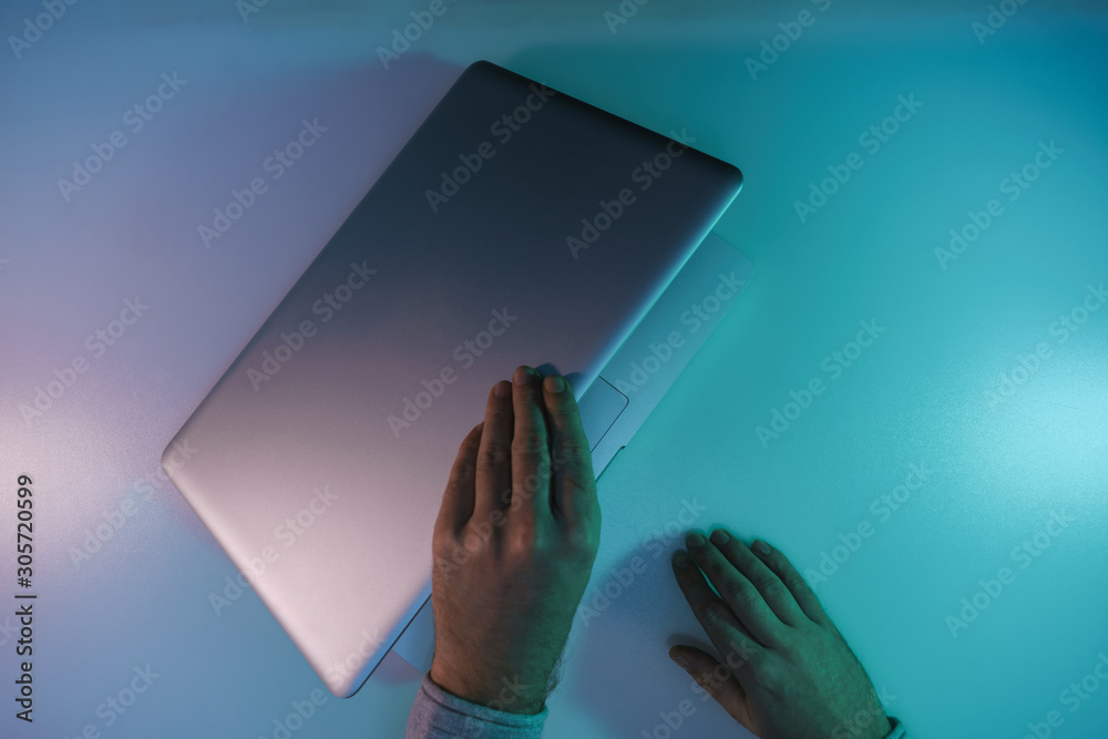 Aufkleber man open silver laptop night online in the color light on a table night background. top view.