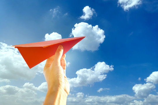 Hand Holding A Red Paper Airplane With Blue Sky