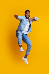 Fototapeta na wymiar Funny afro guy jumping and making karate moves on yellow background