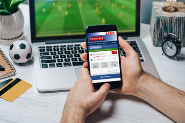 Cropped shot of male fan making bets using gambling mobile application on his phone