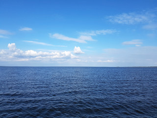 Dark blue sea and sky in the clouds. Bright blue sky with white clouds and calm shining surface of the water in the sea background.