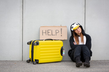 Young woman, with penguin costume and yellow suitcase, has to travel due to global warming. Symbolizes a sad penguin who has to leave his homeland because of global warming or climate change. © epiximages