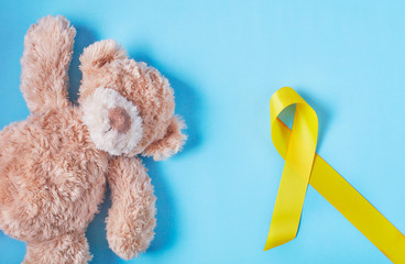 A toy with a yellow Ribbon on light blue background. Childhood Cancer Awareness Yellow ribbon . Childhood Cancer Day February 15. flat lay