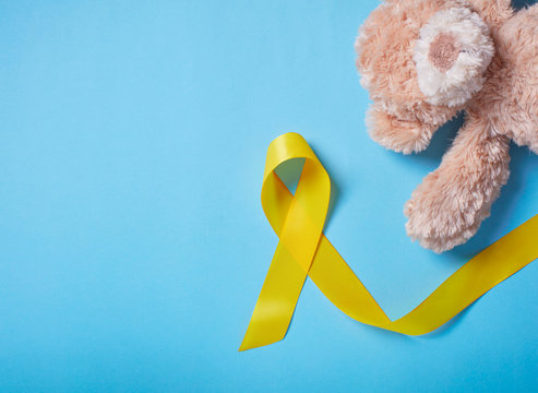 A toy with a yellow Ribbon on light blue background. Childhood Cancer Awareness Yellow ribbon . Childhood Cancer Day February 15. flat lay