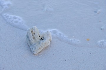 Heart-shape stone on the beach with wave bubbles.
