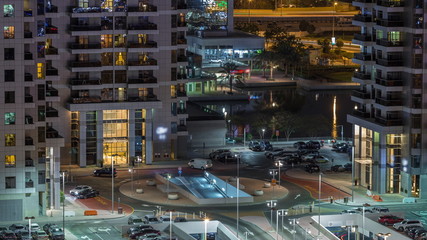 Traffic at parking near entrance to skyscrapers in Jumeirah Lakes Towers night timelapse.