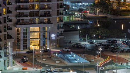 Traffic at parking near entrance to skyscrapers in Jumeirah Lakes Towers night timelapse.