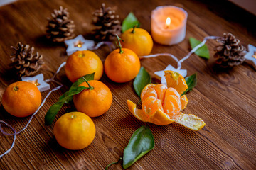 Christmas and new year decor. Christmas card. Tangerines, candle, lights, cones on a wooden background