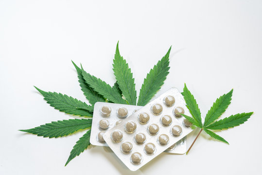 pills made from natural ingredients lie on the leaves of medical marijuana on a white background