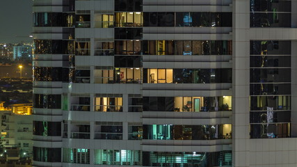 Fototapeta na wymiar Rows of glowing windows with people in apartment building at night.