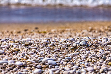 Background of white sea pebbles on the beach. Selective focus, blurred sea waves on background. Sea gravel texture background. Ocean beach vacation concept