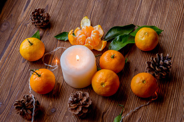 Christmas and new year decor. Christmas card. Tangerines, candle, lights, cones on a wooden background