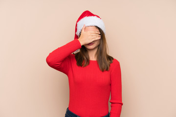 Young girl with christmas hat over isolated background covering eyes by hands