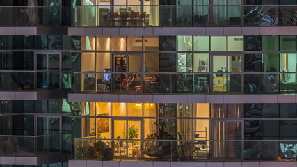 Rows of glowing windows with people in apartment building at night.