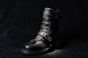 black leather boot with buckles and laces on a dark background.