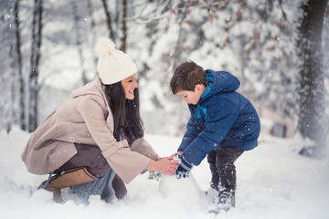 Fototapeta na wymiar Young, beautiful mom and her cute little boy playing in the snow, enjoying winter