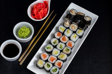 Sushi with fish, with cucumber, with eel, with avocado. Wrapped in Nori Seaweed. Food for vegetarians. Soy sauce, ginger, wasabi in white bowls. Copy space.