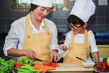  Asian woman young mother with son boy cooking salad mom sliced vegetables food son tasting salad dressing vegetable carrots and tomatoes bell peppers happy family cook food lifestyle kitchen