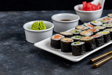Sushi with fish, with cucumber, with eel, with avocado. Wrapped in Nori Seaweed. Food for vegetarians. Soy sauce, ginger, wasabi in white bowls. Copy space.