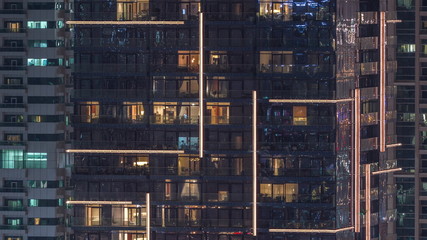 Rows of glowing windows with people in apartment building at night.