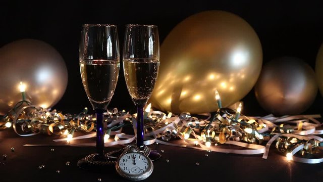The New Year's celebration is about to begin, the champagne effervesces in two flutes against a festive background and the clock reads midnight, 4k