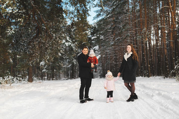 Fototapeta na wymiar mom, dad, daughter and little son having fun in the winter forest. Active parents with children run in the snowy forest