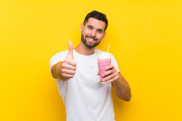 Young man with strawberry milkshake over isolated yellow background with thumbs up because something good has happened