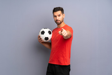 Handsome young football player man over isolated white wall points finger at you with a confident...
