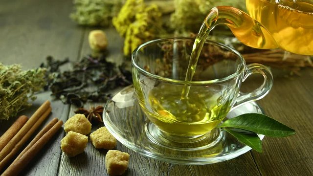 green tea is pouring from a teapot into glass cup