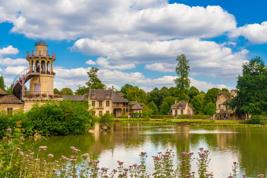 Beautiful panoramic landscape view of the Marlborough Tower, the Queen&rsquo;s House, the boudoir and the mill from the lake in the Queen&rsquo;s Hamlet at the Petit Trianon park of Versailles on a summer day.