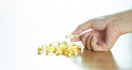 Fish oil capsule in hand on wooden table and white background,supplement with omega3 and vitamin D benefits for support heart health,healthy diet concept, selective focus