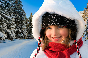 Portrait of happy young girl sitting in the snow with ski in winter time, ski slope in the background.