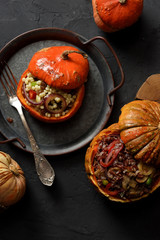 Healthy vegan food. Small orange pumpkins stuffed with red rice, mushrooms, leek, peppers, giant couscous and raisins on vintage metal tray on black background
