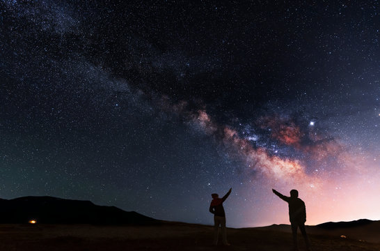 Beautiful night landscape. Two silhouettes stand on a hill and look at the bright galaxy Milky Way